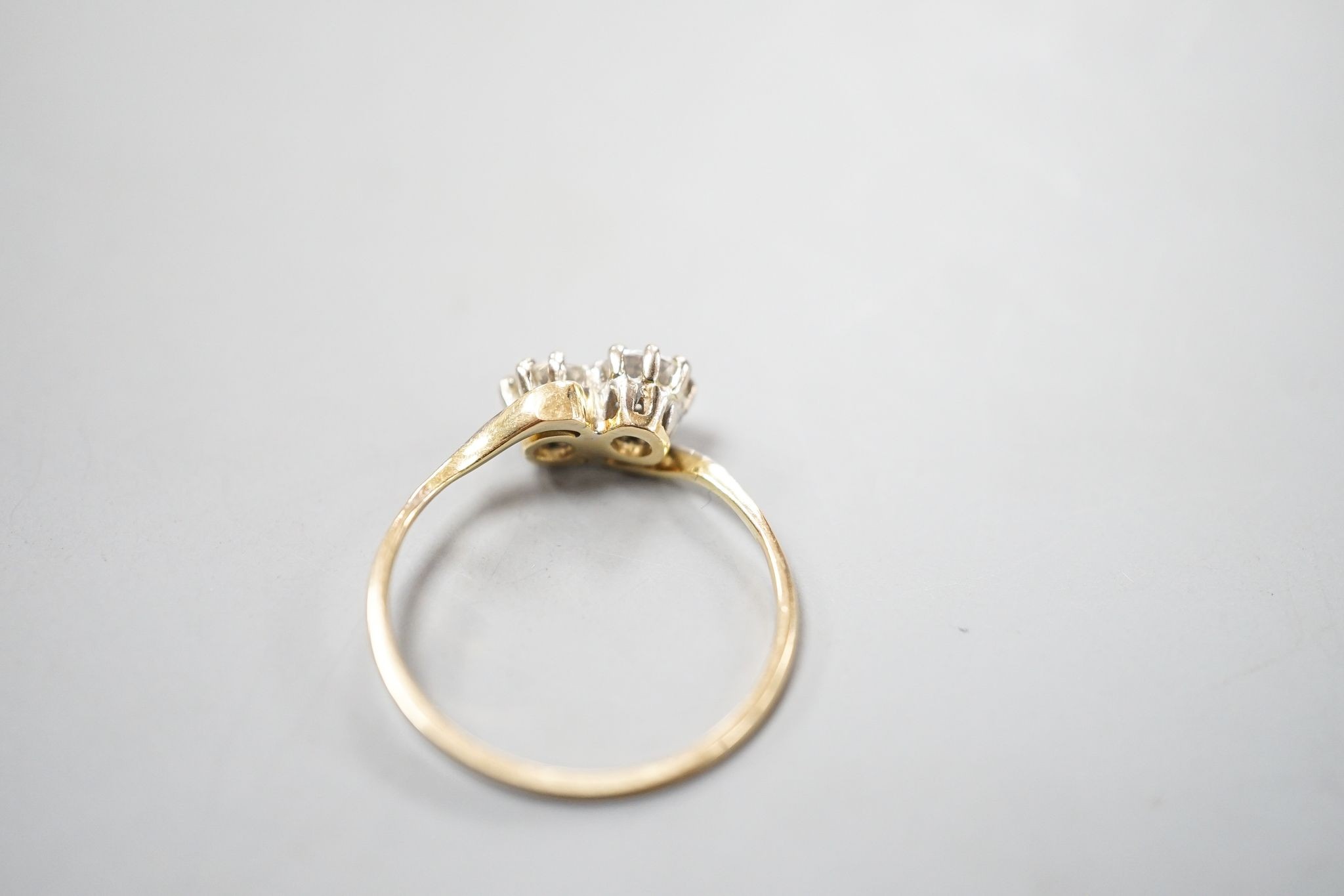 A yellow metal and two stone diamond set crossover ring, size P/Q, gross weight 1.9 grams.